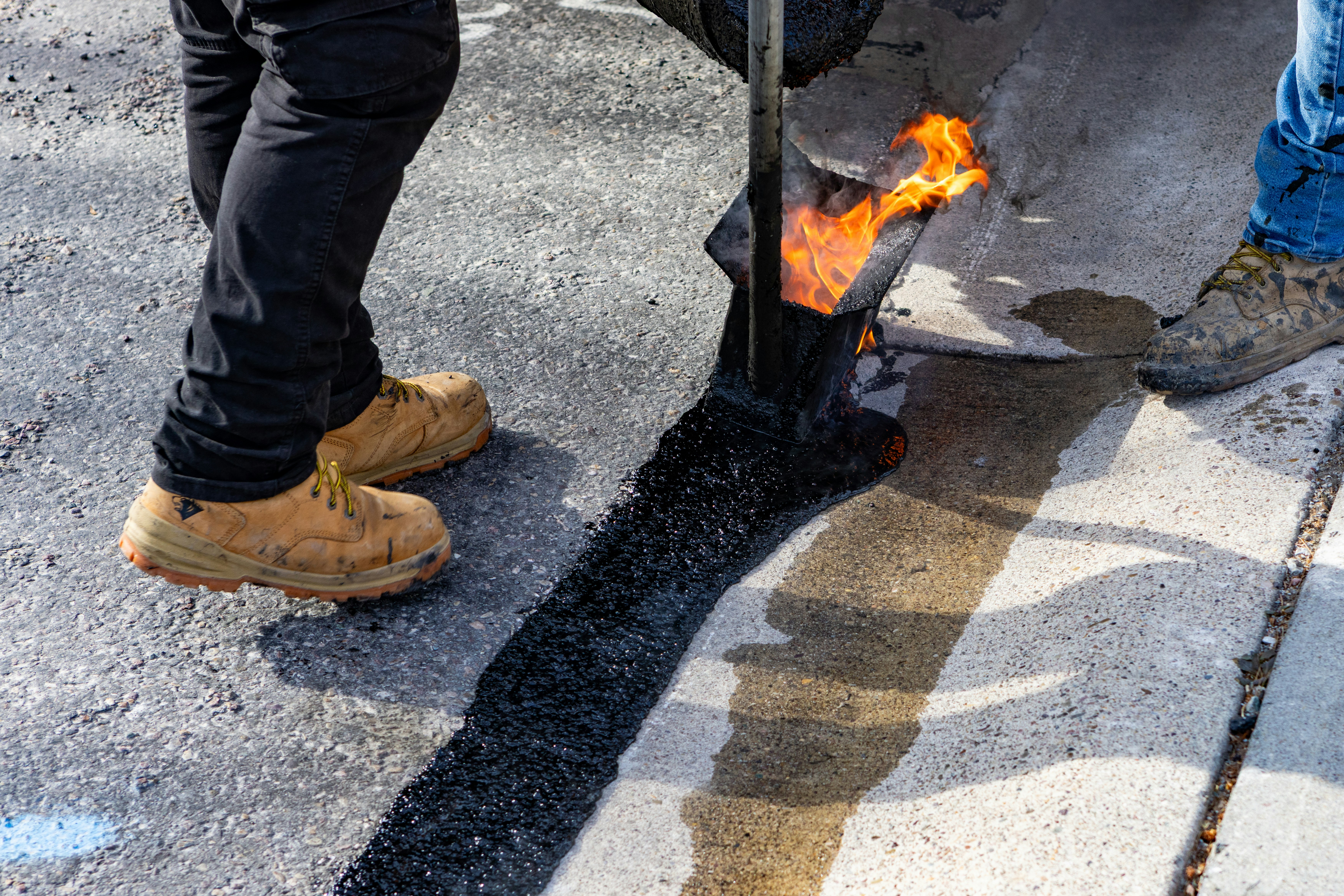 Worker applying hot-pour crack sealant to repair an asphalt surface.