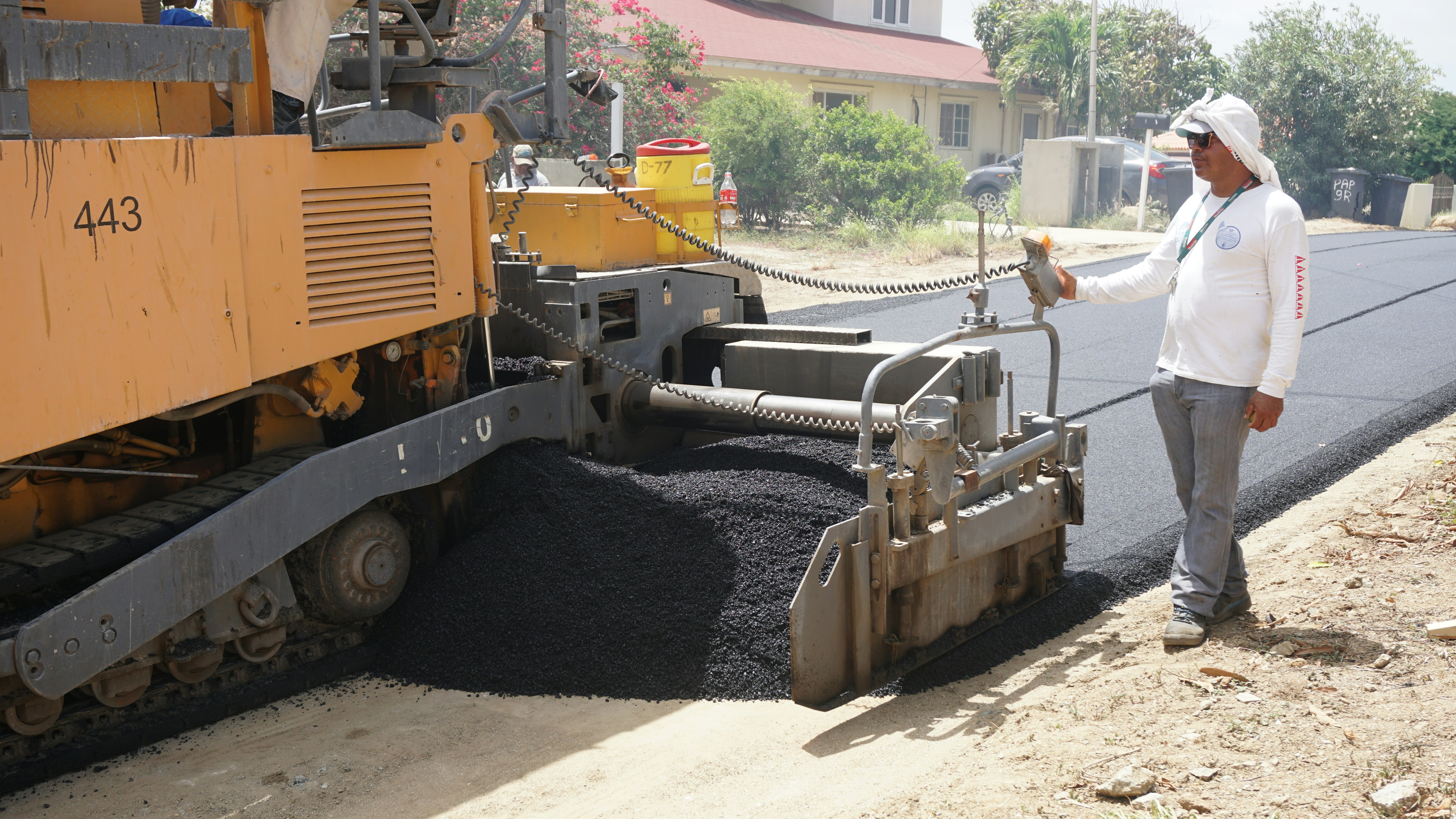 Crew laying fresh asphalt with a paver machine on a new roadway.